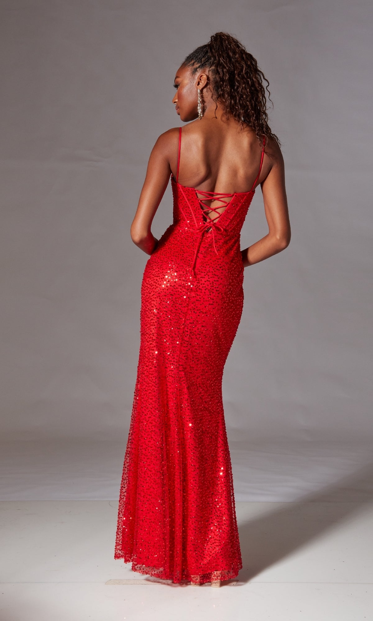 Woman wearing the Corset Long Sequin Prom Dress: Aerie Couture 221—a fitted, floor-length red gown with spaghetti straps, corset-style bodice, and lace-up back—standing against a plain background.